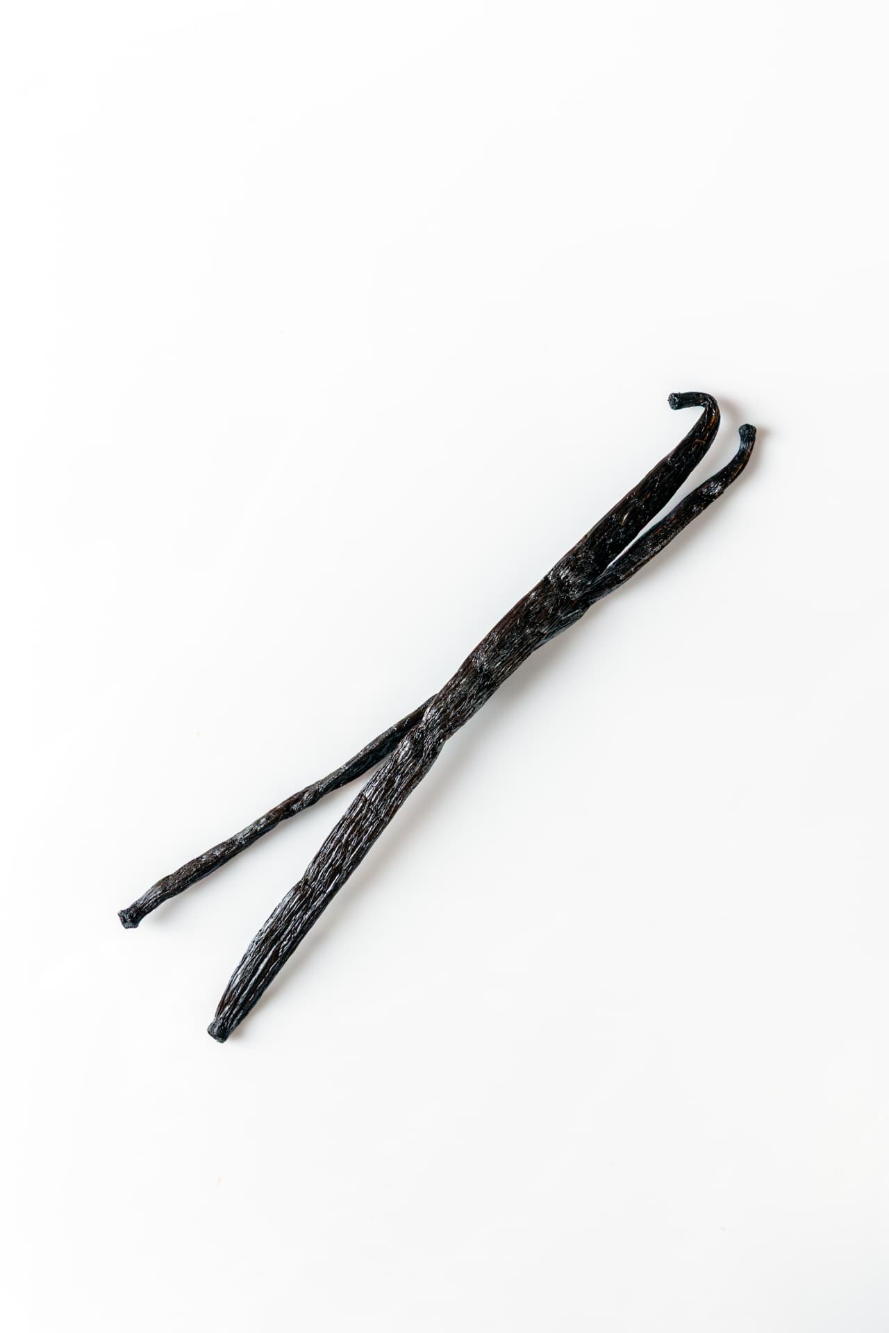 Two dark vanilla pods on a white surface