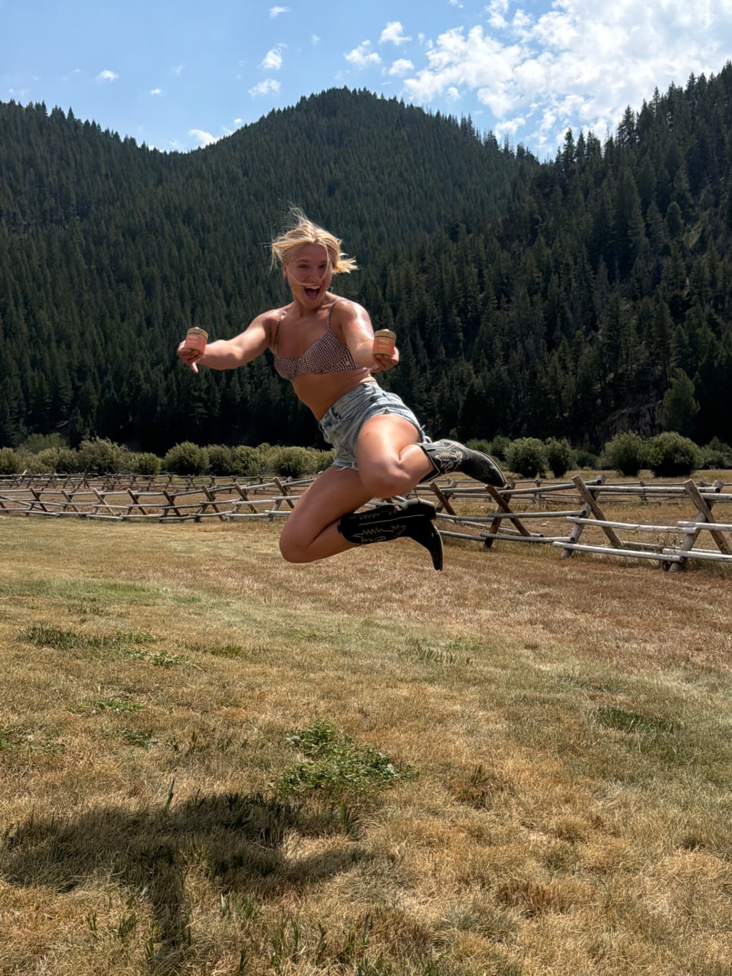 Zoe holding Radiant & Real balm while jumping in an Idaho meadow