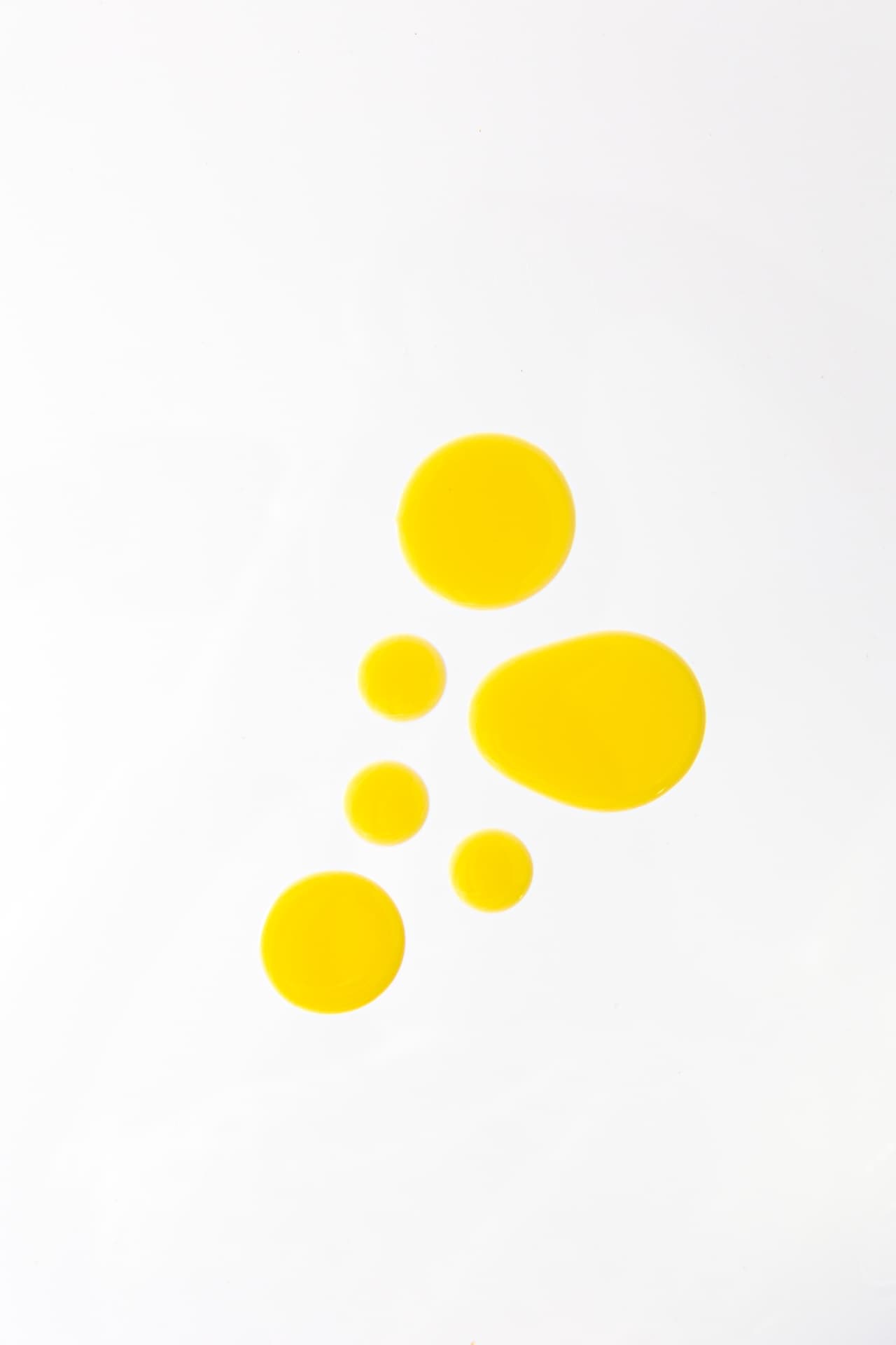 Golden oil droplets on a white surface, illustrating the formula’s botanical oils