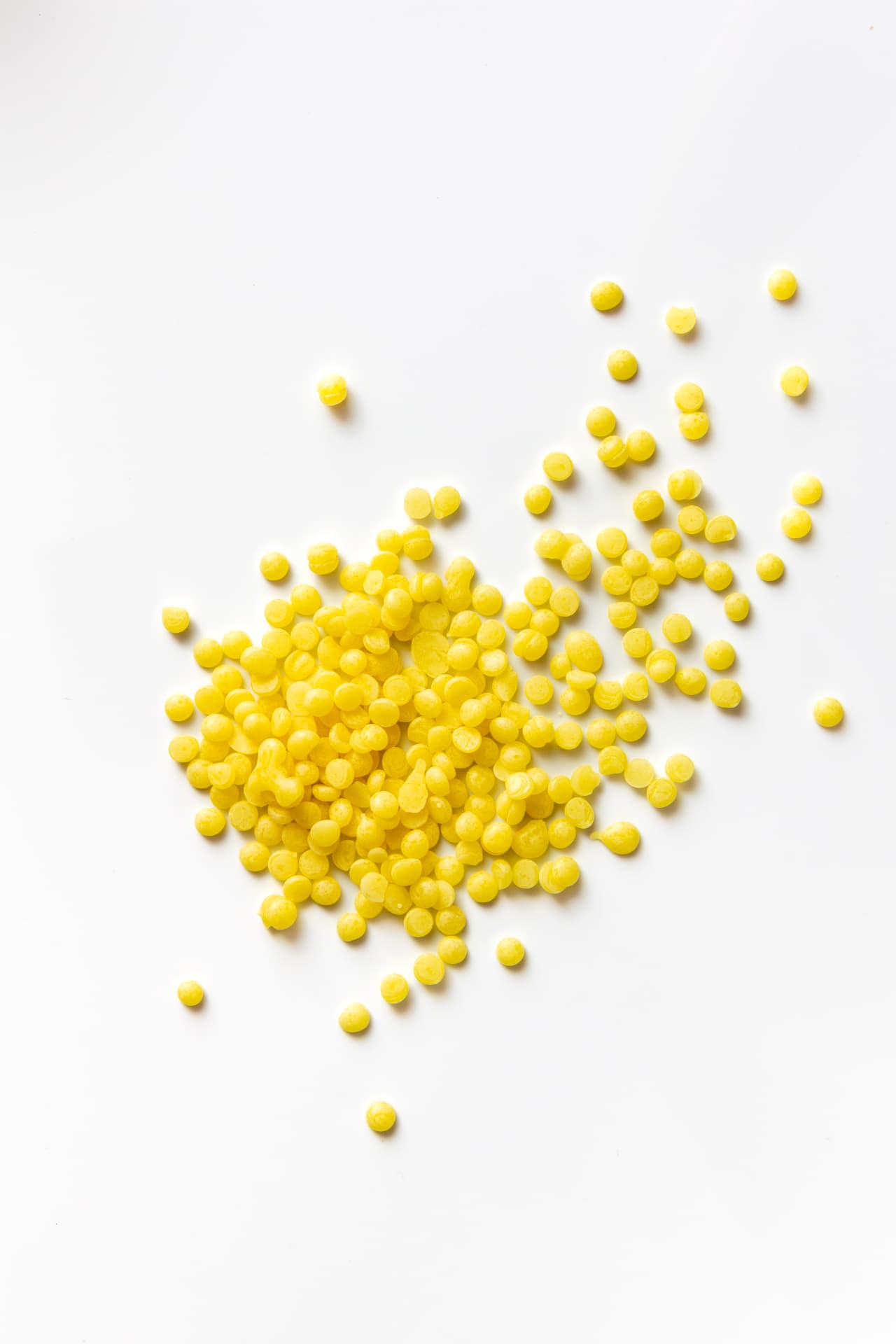 Small yellow beeswax beads scattered across a white surface